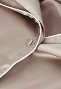 Satin tyg i en taupe-färg med en slät textur, med vit piping och en matchande knappdetalj på framsidan.