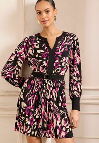 Haljina s cvjetnim uzorkom, dugim rukavima, V-izrezom i strukom naglašenim pojasom. Sadrži ružičaste, crne i krem boje s detaljima od nabora.