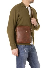 Borsa a tracolla in pelle marrone con forma rettangolare, tasca frontale con zip e tracolla regolabile. Superficie testurizzata con dettagli di cucitura.