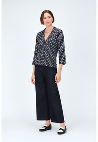 Blusa a righe in bianco e nero con scollatura a V, maniche a tre quarti e bottoni, abbinata a jeans a gamba larga scuri e scarpe nere.