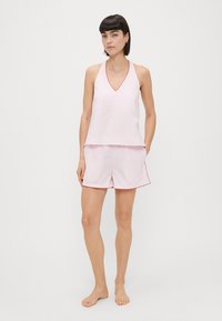 Ensemble de pyjama rose clair comprenant un débardeur à col en V et un short. Détails en piping rouge sur les bords. Tissu doux, coupe relaxée.