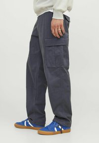 Mørkegrå cargo-bukser med flere lommer, en løs pasform og kontrastsyet. Sammen med blå sneakers med hvide detaljer.