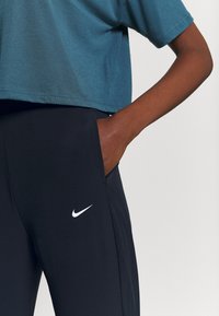 Geknipt teal t-shirt met korte mouwen, gecombineerd met strakke zwarte broek met een wit Nike-logo en zijzak. Soepele stoftextuur.