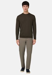 Suéter de manga larga verde oscuro con cuello redondo, combinado con pantalones gris claro y zapatos oscuros. El corte es relajado con una textura suave.