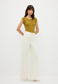 Senapsgul, ribbad croptop ihop med högmidjade, vita vida byxor. Outfitten har en strömlinjeformad design och neutrala nyanser.