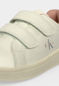 Κοντινό ενός λευκού αθλητικού παπουτσιού Calvin Klein με δύο λουριά με βέλκρο και το λογότυπο CK στο πλάι.