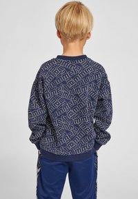 Sweatshirt bleu marine avec un motif logo géométrique blanc. Il présente un col rond et des manches longues, fabriqué en tissu doux mélangé en coton.