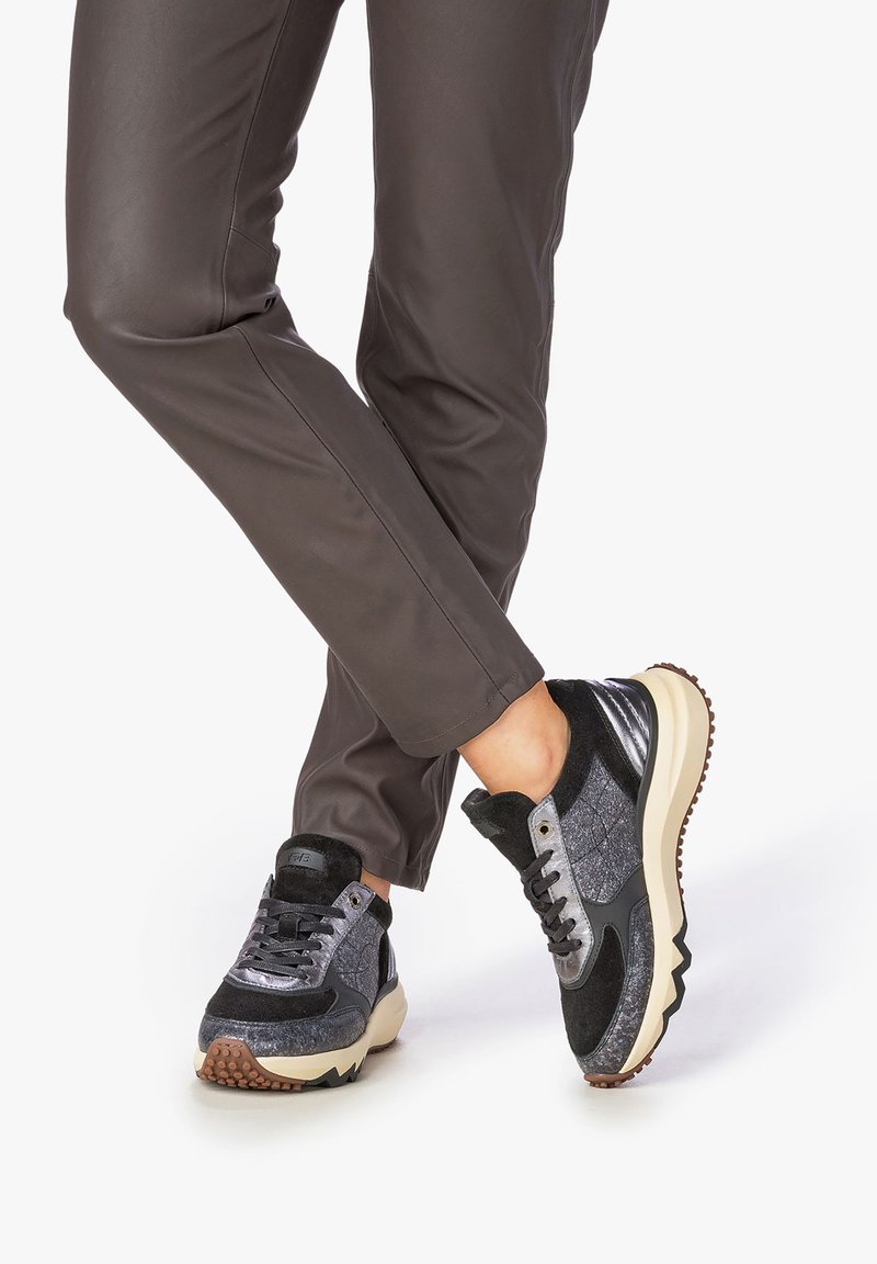 Sneakers sportivi caratterizzati da un mix di materiali testurizzati neri e grigi, con una suola robusta, lacci e un accento di design sottile sul tallone.
