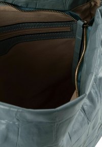 Interno di borsa in pelle azzurro chiaro e texture, con rivestimento beige, tasca con cerniera e rifiniture scure a contrasto.