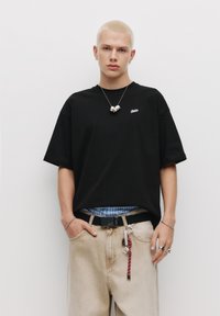 Sort bomulds T-shirt med korte ærmer og et lille logo, parret med lys beige denim jeans og lagdelt med en blå ternet skjorte.