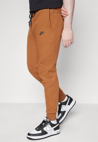 Nike trenirke u smešnoj boji, s elastičnim pojasom i crnom vezicom, bočnim dzepovima i suženim nogavicama. Uparene s crno-belom obućom.