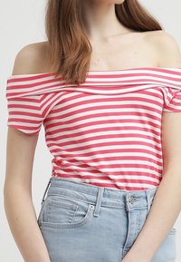 Růžovo-bíle pruhovaný top bez ramínek s krátkými rukávy, vyrobený z měkké tkaniny. Spárováno se světle modrými džíny.