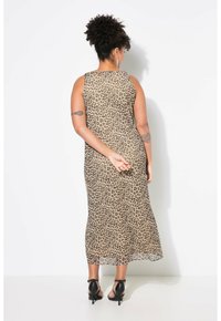 Robe sans manches, arrivant au genou, de couleur beige avec un imprimé léopard noir. Tissu léger, coupe droite et fentes sur les côtés. Portée avec des sandales à talons noires.