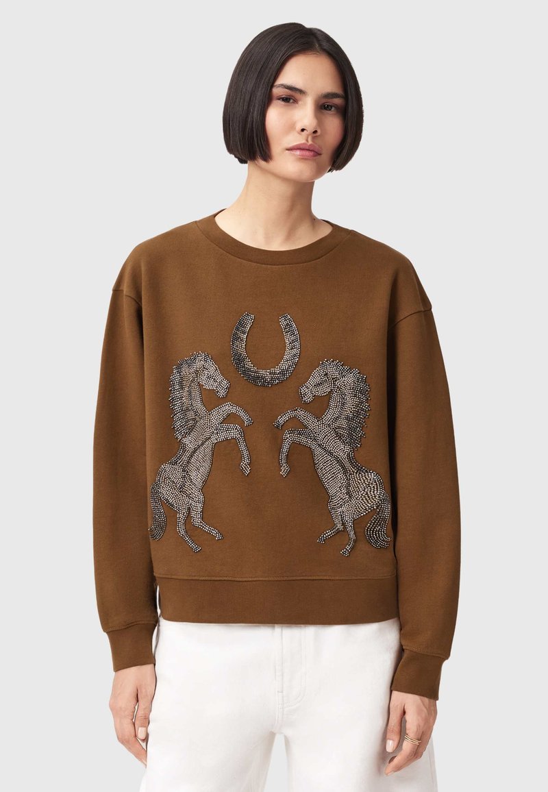 Καφέ φούτερ με σχέδιο δύο ανεβαίνουσων αλόγων και πέταλο από μεταλλικές στρας. Λαιμόκοψη crew και ριμπ μανσέτες με άνετη εφαρμογή.