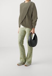 Olivengrøn fleecetrøje med diagonal mønster, kombineret med teksturerede grønne og gule mønstrede bukser samt en sort håndtaske i halvmåneform.