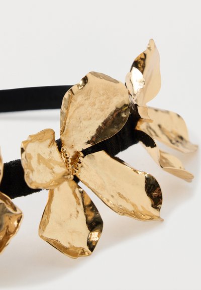 Zlatá kovová květinová čelenka s texturovanými květy na černé elastické pásce, s detaily okvětních lístků a malými korálkovými akcenty uprostřed.