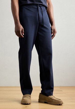 Navyblaue Lounge-Hosen aus weichem Stoff mit einem Gummizugbund, die eine lockere Passform aufweisen und sich zum Knöchel hin verjüngen. Keine sichtbaren Muster.