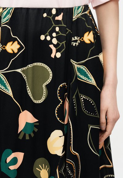 Μαύρη φούστα με αφηρημένα λουλουδάτα και φυλλώδη σχέδια σε πράσινο, μπεζ, ροζ και πορτοκαλί, φορεμένη από άτομο με ανοιχτό ροζ τοπ, με ορατό το χέρι στο πλάι.