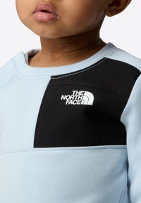 Light blue sweatshirt with a black panel and white logo. Features a crew neckline and soft texture. Includes contrasting stitching details.