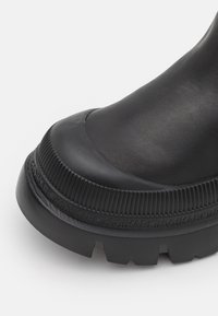 Schwarze Knöchelstiefel mit einem glatten Lederoberteil, runder Zehenform, strukturiertem Gummisohle mit einem gerippten Design und eingeprägtem Branding um die Sohle.