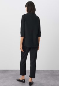 Zwart, langmouwig shirt met een ronde halslijn, gedragen met zwarte, rechte broek. Beide kledingstukken zijn gemaakt van een gladde stof.