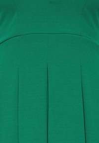 Grön klädestyg visar en texturerad, slät yta med vertikala veck och en strukturerad design som framhäver en elegant silhuett.