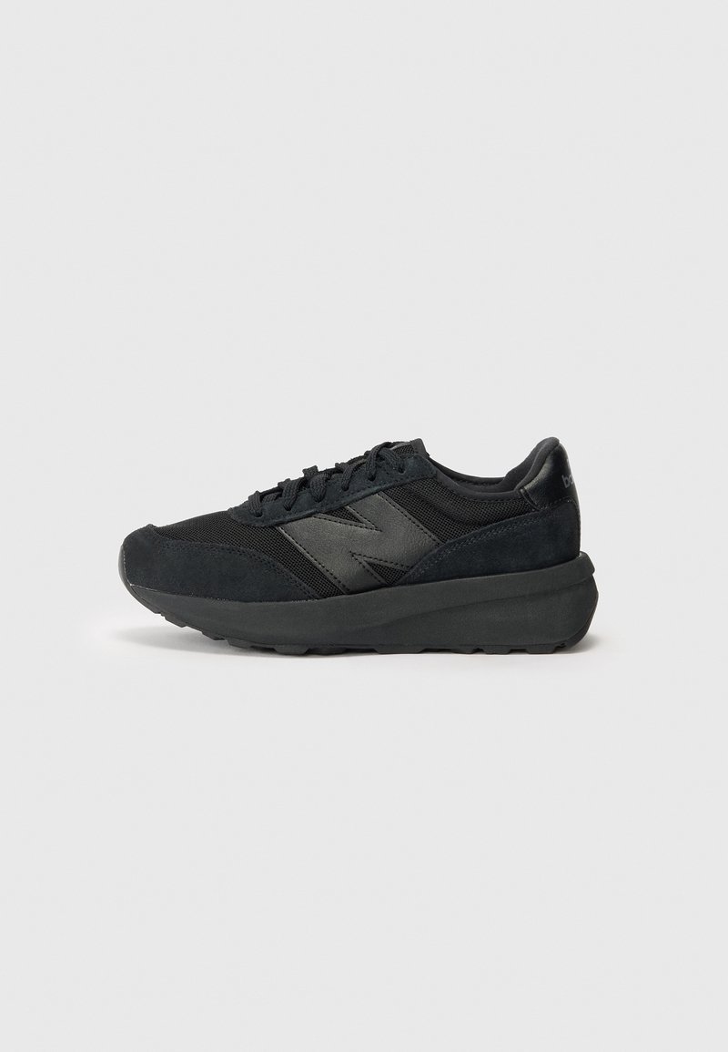 Chaussures de sport noires avec une tige en daim et en mesh, présentant un bout arrondi, une semelle intercalaire proéminente et un design minimaliste avec un accent de logo.