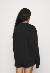 Černá mikina s kulatým výstřihem, dlouhými rukávy a volným střihem, se žebrovanými manžetami a lemem, zobrazená zezadu.