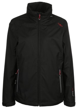 Persoon draagt een zwarte waterdichte jas met capuchon, zwarte broek en zwarte wandelschoenen en staat tegen een effen lichte achtergrond.