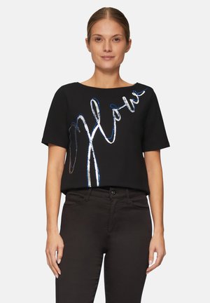 Haut noir à manches courtes avec un design ondulé en argent métallisé et bleu "Wow". Tissu lisse avec une coupe ample. Associé à un pantalon sombre.