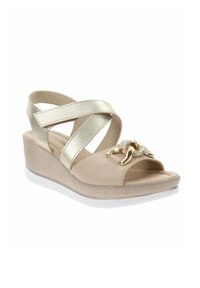 Sandali con zeppa beige, con cinturini incrociati in metallo dorato, punta aperta e dettaglio decorativo in catena dorata. Superficie morbida con una suola bianca.