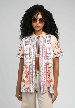 Chemise à manches courtes en tissu beige avec des motifs floraux et animaux rouges et bleus, dotée d'un devant boutonné et d'un col.