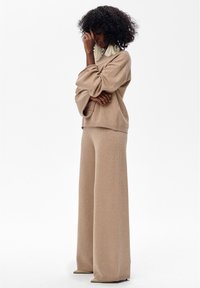 Beige gebreide trui en broek met wijde pijpen en een zachte textuur. De outfit heeft een ontspannen pasvorm en een subtiele glans.
