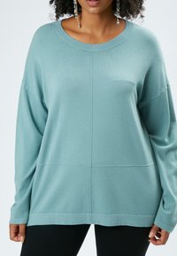 Maglione verde acqua realizzato in materiale morbido, con una vestibilità ampia, maniche lunghe e un collo a costine con dettagli a pannello discreti.