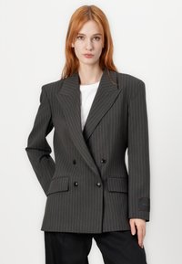 Karbonsko sivo dvoredno blejzer s pinstripi, širokimi reverji, gumbi in stranskimi žepi. Nosi se čez belo srajco.