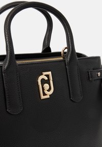 Czarna skórzana torebka z złotymi akcentami, teksturowanym wykończeniem, dwoma okrągłymi uchwytami oraz zamkiem błyskawicznym z detalem logo.