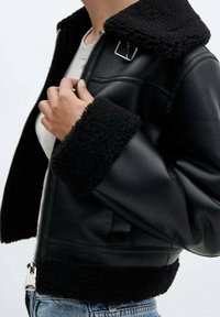 Giacca nera in pelle con collo e polsini in ecopelliccia; presenta una cerniera frontale e dettagli decorativi in metallo. Vestibilità casual e texture.