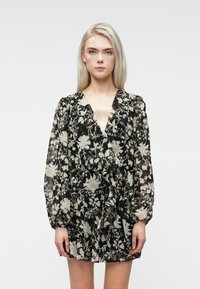 Vestito nero floreale con motivi crema, maniche lunghe, scollatura a V profonda, vita cintrata e gonna fluida in un tessuto leggero.