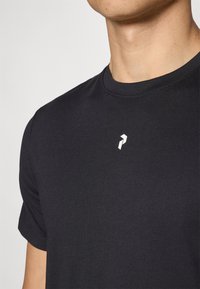 Sort kortærmet bomulds T-shirt med rund halsudskæring og et lille hvidt logo på brystet. Glat tekstur, tætsiddende design.