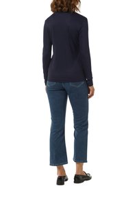 Marineblaue Langarmbluse aus weichem Material, kombiniert mit hellblauen geraden Jeans, klassischen Taschen und schwarzen Slippers.