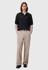 Svart kortärmad polo med en strukturerad stickad design, kombinerat med beige raka byxor och svarta skor. En enkel, ren estetik.