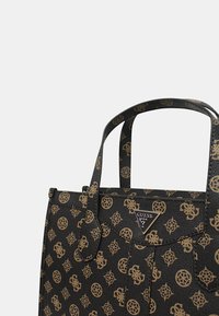 Sac fourre-tout noir avec une finition texturée, affichant un logo doré et des motifs géométriques répétitifs. Deux poignées robustes pour le transport.