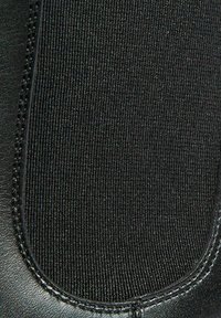 Zapato híbrido de cuero negro y tejido que presenta una textura suave, panel superior elástico y detalles de costura a lo largo de los bordes.