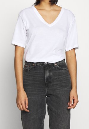 Weißes Baumwoll-T-Shirt mit V-Ausschnitt und kurzen Ärmeln, kombiniert mit hoch taillierten dunkelgrauen Denim-Jeans mit Fronttaschen und einem used Look.