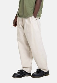 Beige wide-leg pants with a smooth texture, paired with black leather shoes featuring a tassel detail. The top is olive green and casual.