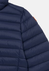 Marine blafjærjakke med kviltet design, høy krage og oransje detaljer på skulderen. Materialet ser glatt og isolert ut.