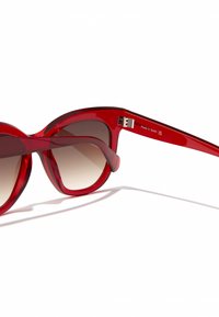 Piros napszemüveg túlságosan nagy, macskaszem alakú, fényes műanyag kerettel, barna árnyalatos lencsékkel és ezüst fém díszítéssel a szártól.