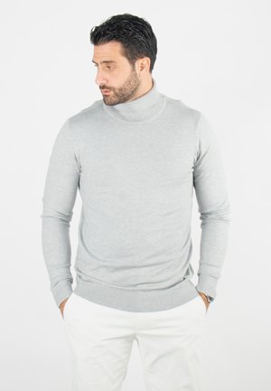 Un pull col roulé gris clair en tissu doux avec des manches longues ajustées et un col et des poignets côtelés, associé à un pantalon blanc.