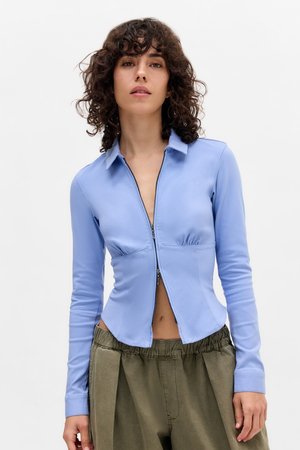 Camisa de cremallera de color azul claro con cuello, diseño ajustado, cintura fruncida y mangas largas, combinada con pantalones verdes de cintura elástica.