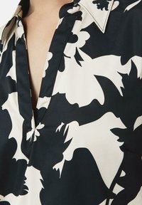 Camicia con motivo floreale in bianco e nero, con colletto, che presenta una profonda scollatura a V e una texture del tessuto liscia. Dettagli distintivi nella pattina.